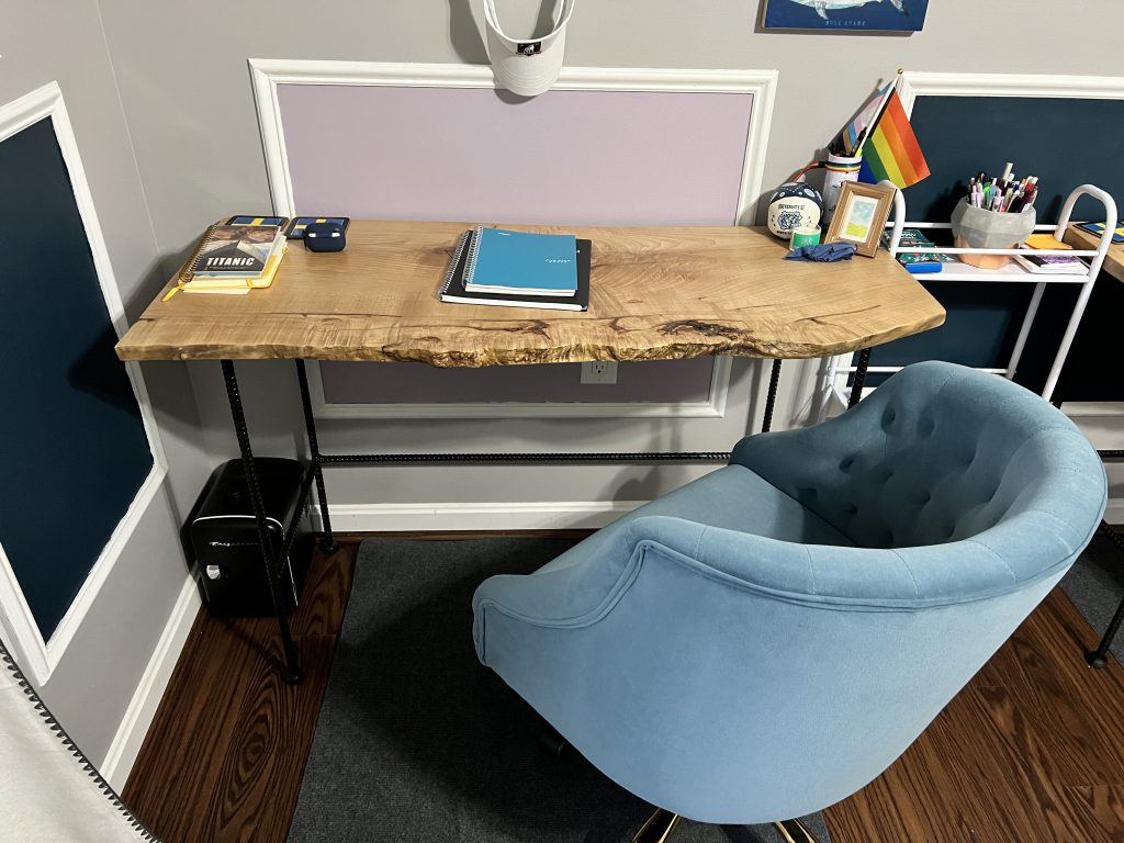 A desk made by Shenandoah Primitives with a few notebooks and a blue velvet chair